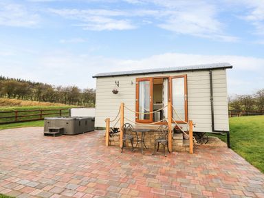 A small cabin with open double doors a metal table and two chairs on a paved area at Highland View in Rhayader