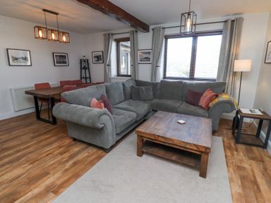 A living room with a gray sectional sofa wooden coffee table dining table with chairs and framed pictures on the wall at The Old School in Lowick