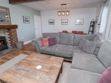 A living room with a grey sectional sofa and wooden coffee table near a fireplace and dining area at The Old School in Lowick
