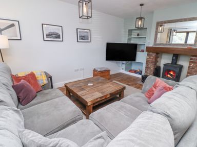 A living room with grey sofas and a wooden coffee table a fireplace with a fire and a wall-mounted television at The Old School in Lowick