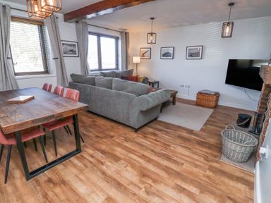 A living room with a gray sofa and a wooden dining table with red chairs at The Old School in Lowick