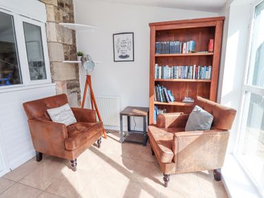 A small seating area with two brown armchairs and a wooden bookshelf at The Old School in Lowick