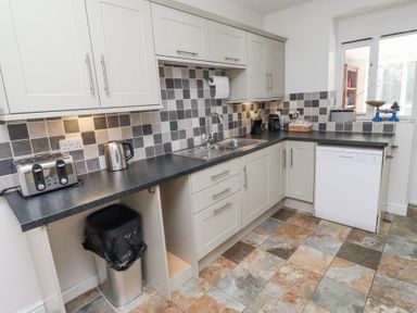 A kitchen with tiled backsplash a sink dishwasher toaster kettle trash bin and cabinets at The Old School in Lowick