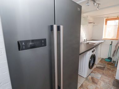 A utility room with a gray fridge freezer stainless steel sink washing machine and cleaning tools at The Old School in Lowick
