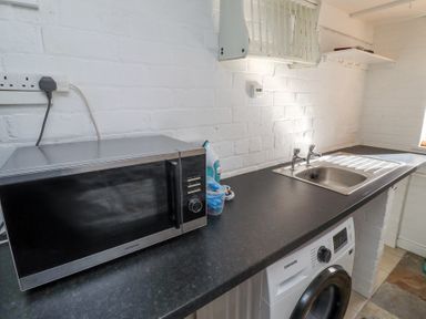A kitchen counter with a microwave iron sink and washing machine at The Old School in Lowick