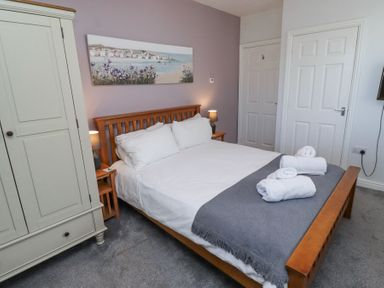 A bedroom with a wooden bed frame white bedding grey blanket white towels on bed two bedside tables with lamps and a white wardrobe at The Old School in Lowick