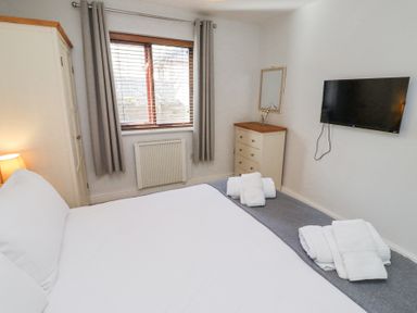 A bedroom with a bed towels on the floor a chest of drawers a wall-mounted TV and a window with curtains at The Old School in Lowick