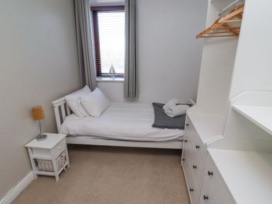 A small bedroom with a single bed bedside table lamp and dresser with hangers at The Old School in Lowick