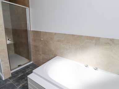 A bathroom with a white bathtub and a tiled shower enclosure at The Old School in Lowick