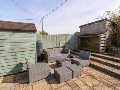 An outdoor patio with grey wicker furniture including chairs a sofa and tables near wooden sheds and a fence at The Old School in Lowick