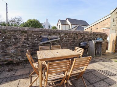 An outdoor patio area with a wooden table and six chairs a barbecue and a stone wall at The Old School in Lowick