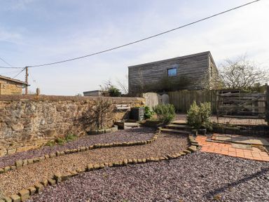 An outdoor area with a stone wall gravel paths small plants wooden fences and a wooden building in the background at The Old School in Lowick