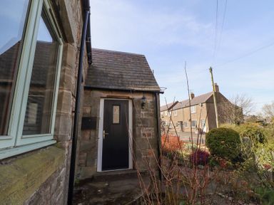 A stone exterior wall with a black door and window beside a garden with shrubs at The Old School in Lowick