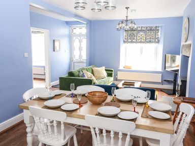 A dining room with a wooden table set with plates and glasses and a living room with a green sofa and a television at Estcote Roger Ground near Hawkshead