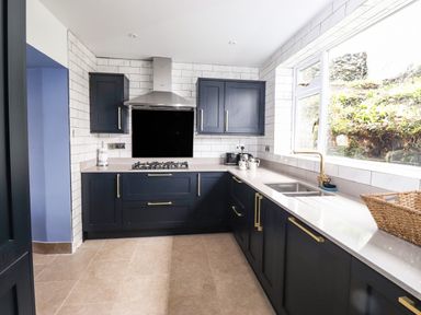 A kitchen with dark cabinets a gas stove a sink under a window and a woven basket on the counter at Estcote Roger Ground near Hawkshead