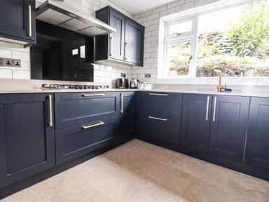 A kitchen with dark blue cabinets brass handles a gas stove a window and a beige tiled floor at Estcote Roger Ground near Hawkshead
