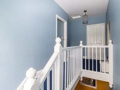 A hallway with blue walls white railing and doors and a basket on the floor at Estcote in Roger Ground near Hawkshead