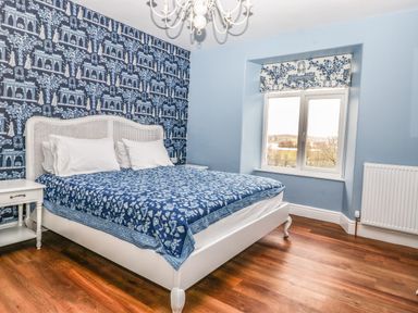 A bedroom with a white bed and blue bedspread near a window with a patterned roman blind at Estcote Roger Ground near Hawkshead