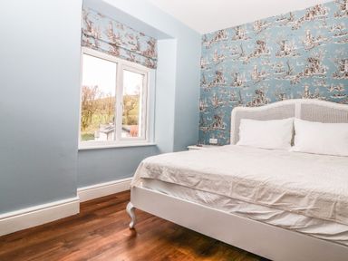A bedroom with a white bed next to a window and blue patterned wallpaper at Estcote Roger Ground near Hawkshead