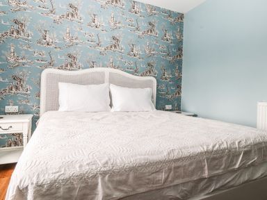 A bedroom with a bed with white bedding and pillows and patterned blue wallpaper at Estcote Roger Ground near Hawkshead