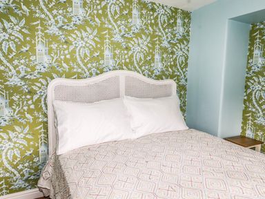 A bed with a white wicker headboard and patterned quilt against a green floral wallpapered wall at Estcote Roger Ground near Hawkshead