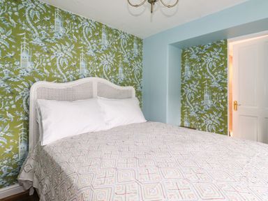 A bedroom with a bed with white pillows and patterned bedspread and green floral wallpaper at Estcote Roger Ground near Hawkshead