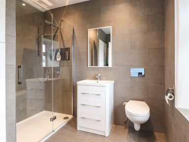 A bathroom with a glass shower enclosure a white sink with drawers a wall-mounted toilet and a mirror at Estcote Roger Ground near Hawkshead