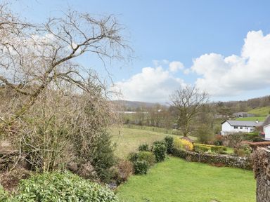 A rural garden with trees bushes and stone walls near white houses and rolling hills at Estcote Roger Ground near Hawkshead