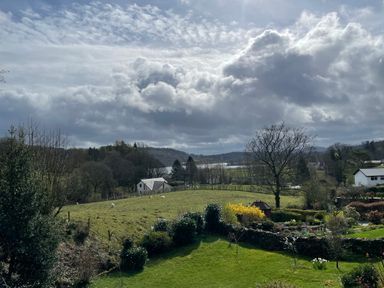 A rural landscape with grassy fields trees and houses under a cloudy sky at Estcote Roger Ground near Hawkshead