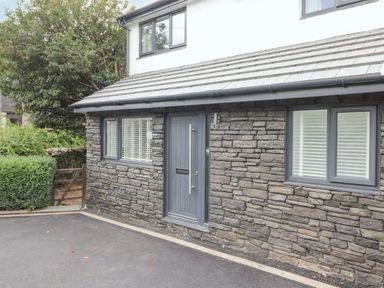 The exterior front of a stone house with a grey door and windows with white blinds