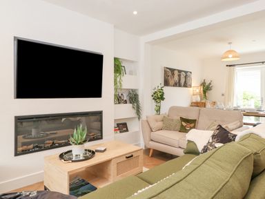 A living room with a wall-mounted television above a fireplace and green and beige sofas at Rydal Rock in Ambleside