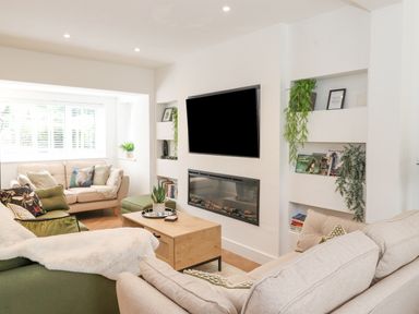 A living room with sofas a coffee table a wall-mounted television and built-in shelves with plants and books at Rydal Rock in Ambleside