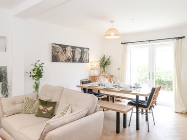 A dining area with a wooden table set for meal and a beige sofa with cushions in a room with white walls at Rydal Rock in Ambleside