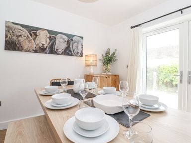 A dining room with a set table with white dishes and glassware a painting of sheep on the wall and a wooden cabinet with plants at Rydal Rock in Ambleside