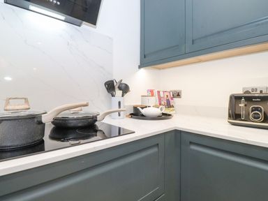 A kitchen corner with blue cabinets a stovetop with pots kitchen utensils cookbooks a teapot and a toaster at Rydal Rock Ambleside