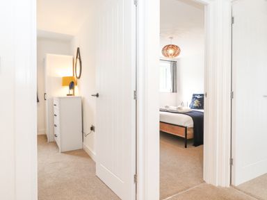 A hallway with open white doors showing a bedroom with a bed and a dresser with a lamp at Rydal Rock in Ambleside