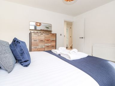 A bedroom with a bed with blue and gray pillows white towels on navy blue runner and a wooden dresser with a mirror at Rydal Rock in Ambleside