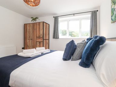 A bedroom with a made bed with blue and gray pillows a wooden wardrobe and a window with gray curtains at Rydal Rock Ambleside