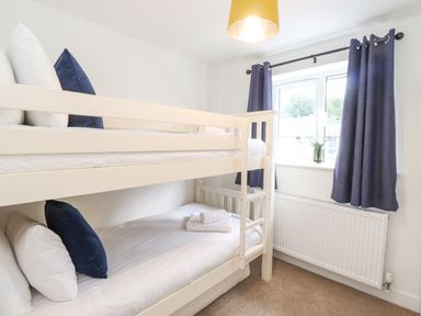 A bedroom with a white bunk bed blue pillows a window with blue curtains and a radiator below at Rydal Rock in Ambleside
