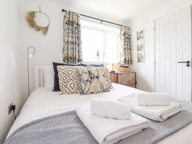 A bedroom with a bed with patterned pillows and folded towels on it next to a window with curtains and a wooden drawer at Rydal Rock in Ambleside