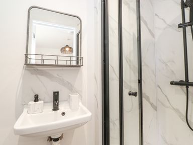 A bathroom sink with soap dispenser and cup next to a shower with black framed glass door at Rydal Rock in Ambleside