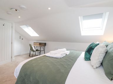 A bedroom with a bed, green pillows, a green bedspread, folded towels, a desk with a chair, skylight windows at Rydal Rock in Ambleside