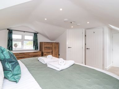A bedroom with a bed with green bedding folded towels on the bed wooden dresser and wardrobe two white doors and a window with green curtains at Rydal Rock in Ambleside