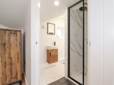 A bathroom with a shower enclosure and sink next to a wooden wardrobe at Rydal Rock in Ambleside