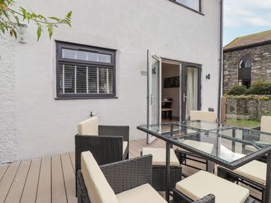 An outdoor patio area with a glass table and cushioned chairs next to a white building with open double doors at Rydal Rock in Ambleside