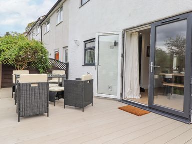 An outdoor patio with rattan chairs and glass table next to a white building with open doors at Rydal Rock in Ambleside