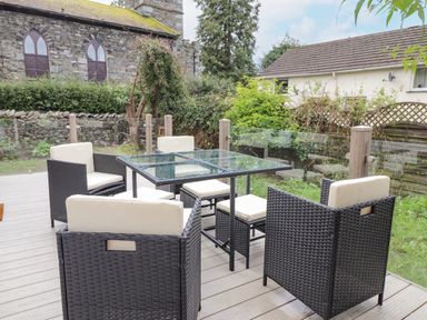 An outdoor patio with a glass table and four chairs with cushions surrounded by glass panels at Rydal Rock in Ambleside