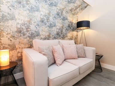 A living room with a two-seater sofa with cushions a floor lamp and a side table with a lamp at Fenty's in Bowness-On-Windermere