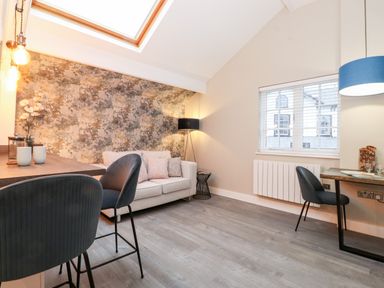 A living area with a sofa, patterned wall, floor lamp, dining table with chairs, and a window with blinds at Fentys in Bowness-On-Windermere