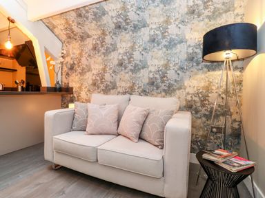 A small living room with a beige sofa with cushions a floor lamp and a side table with magazines at Fenty's in Bowness-On-Windermere